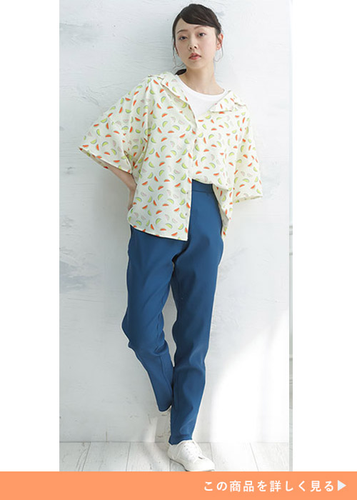 白トップスに黄色の柄シャツを片裾インで重ね、ダークブルーのパンツを履く女性
