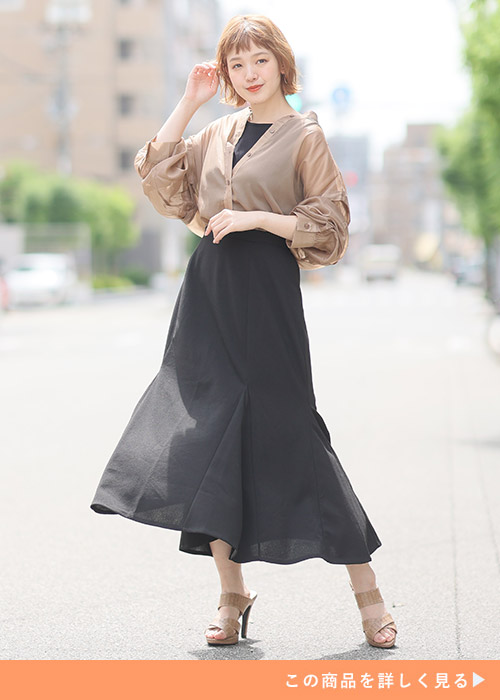 黒のトップス×マーメイドスカートにベージュのシアートップスを着る女性