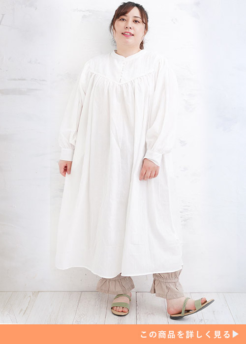 白のシャツワンピースを着て、下にベージュの裾しぼりパンツを履く女性