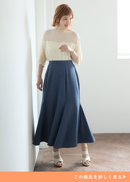 白のシアートップスをブルーのフレアーマーメイドスカートにインして着る女性