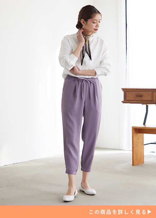 白シャツ×ライラック色のジョガーパンツを着て、首元にスカーフをする女性