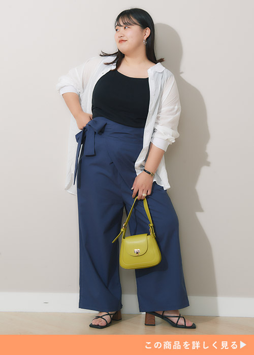 ネイビーのラップパンツに黒トップスをインして、白のシアーシャツを羽織る女性