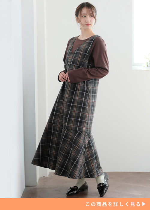 チャコールグレーのジャンスカとブラウンのトップスのコーデに、黒のパンプスを履く女性