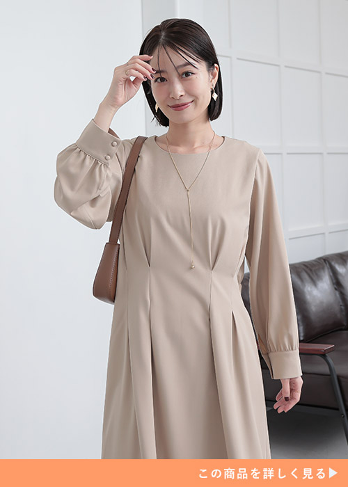 ベージュのタック入りワンピースを着てベージュのバッグを持つ女性