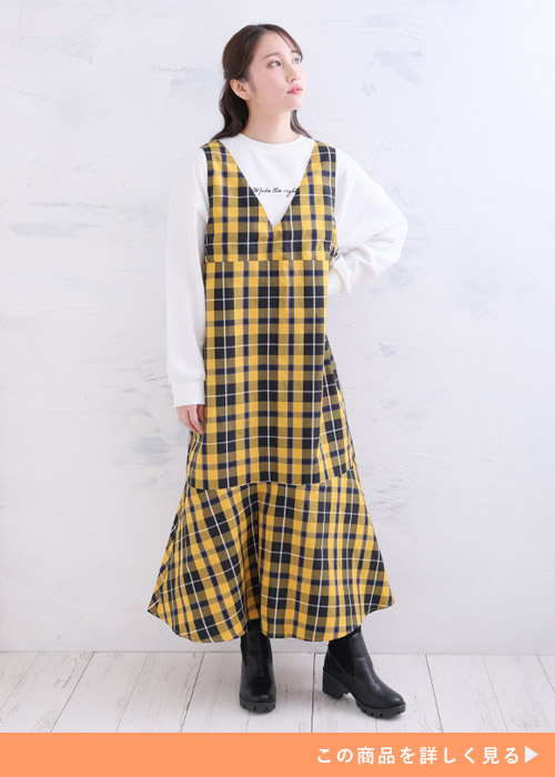 イエローとブラックのチェック柄ワンピとホワイトトップスのコーデに黒いブーツを履く女性