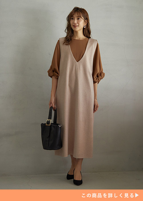 グレージュのVネックワンピースとブラウンのトップスのコーデ、に黒いバッグとパンプスを合わせた女性