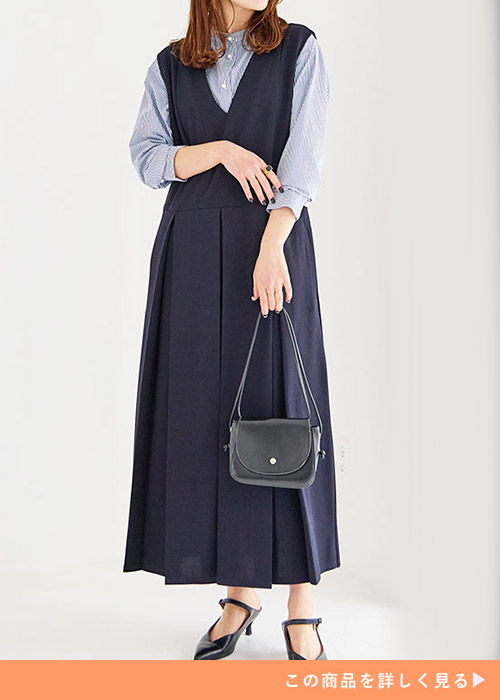 ネイビーのウエストタック入りジャンスカとブラウスのコーデに黒いパンプスを履く女性