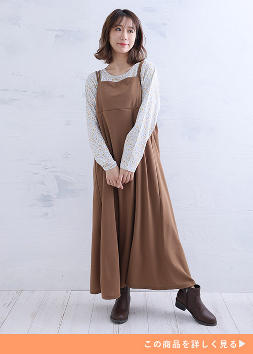 キャメルのキャミワンピースとプリントブラウスのコーデにブラウンのブーツを履く女性