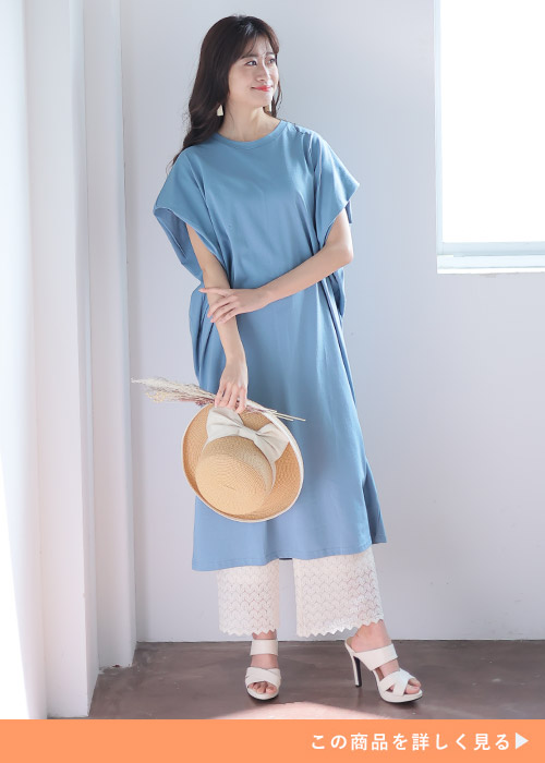 ダスティブルーのドルマンワンピースにホワイトのパンツとサンダルを合わせる女性