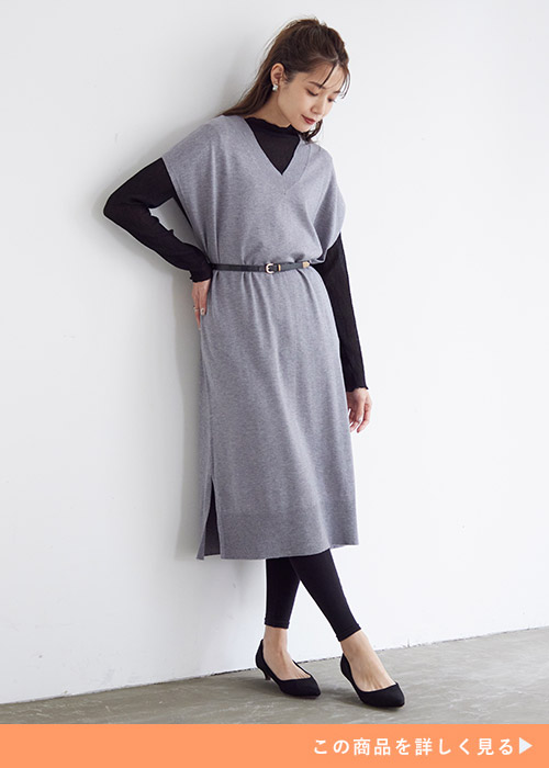 グレーのニットベストワンピースに黒いインナーとレギンス、パンプスを合わせる女性