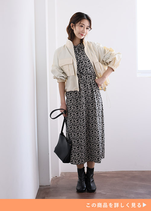 ケープ風デザインの小花柄ワンピースを着て、ブルゾンを羽織る女性。
