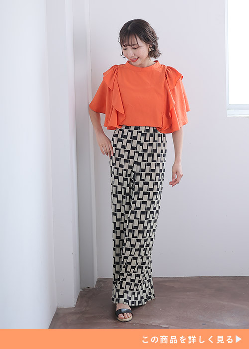 オレンジの袖フリルブラウスを着て、モノトーンの柄パンツを履く女性