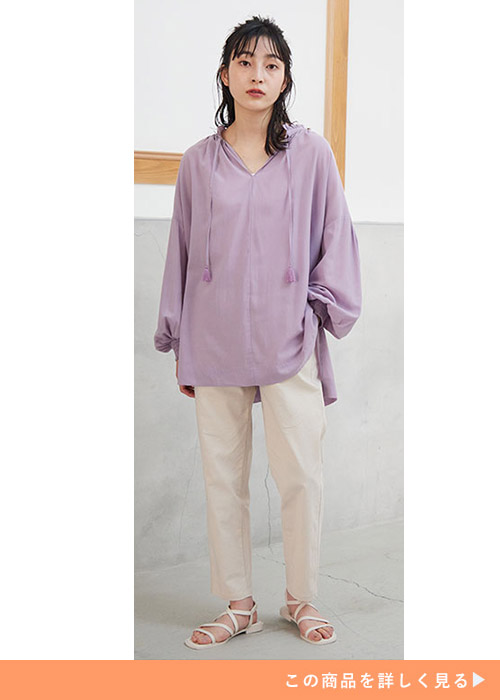 薄いパープルのシアーブラウスを着て、アイボリーのパンツを履く女性。