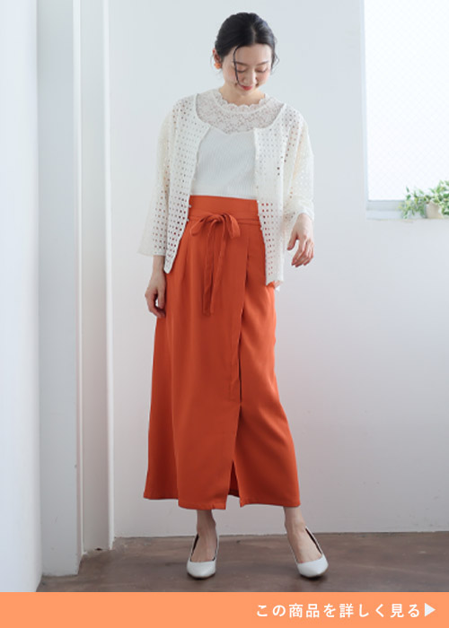 白トップス×オレンジのタイトスカートに、白の透けカーディガンを羽織る女性