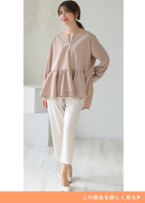 ピンクベージュのペプラムブラウスを着て、白のアンクル丈パンツを履く女性