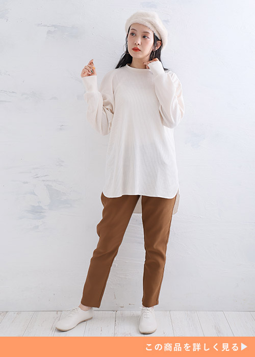 ブラウンのスキニーパンツとゆったりトップスに白のスニーカーを履く女性