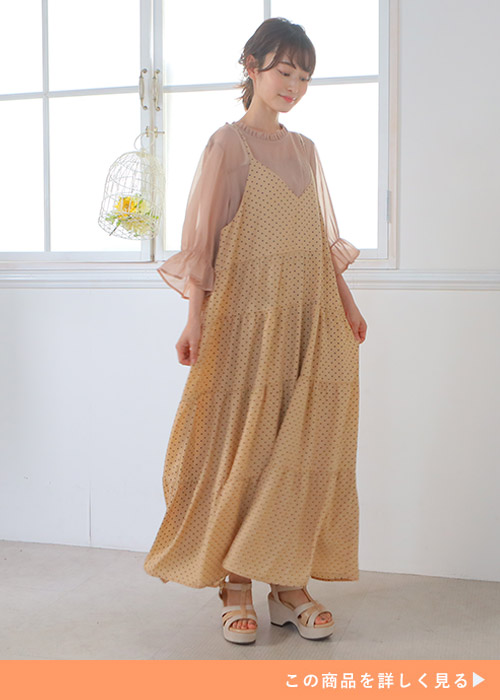 くすみピンクのシアートップスにベージュのドット柄キャミワンピを重ね着する女性