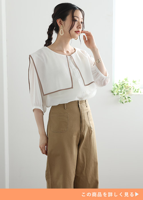 セーラーカラーの白のシャツブラウスを着て、ベージュのパンツを履く女性