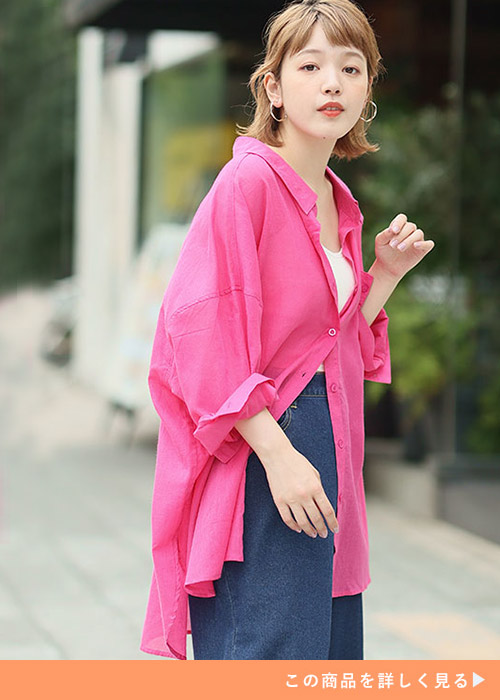 白キャミソールにビビッドピンクのシャツを羽織り、デニムパンツを履く女性