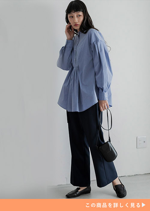 シャンブレーブルーのチュニックシャツを着て、黒のセンタープレスパンツを履く女性
