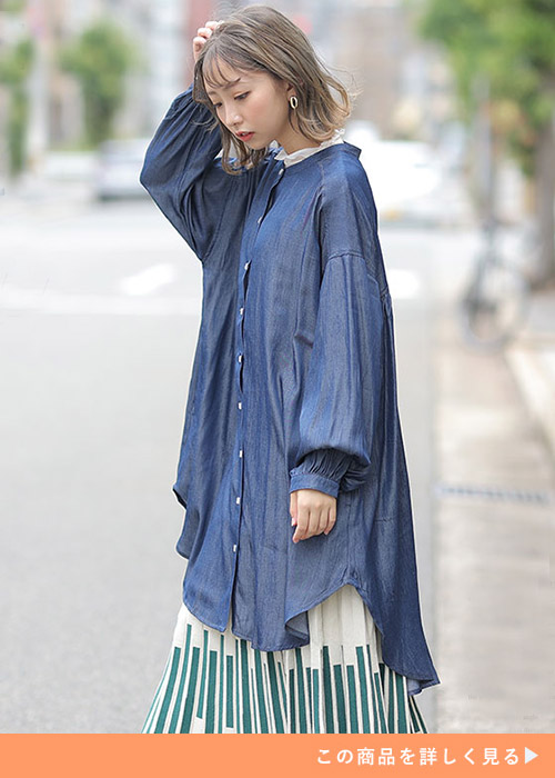 デニム風生地のシャツチュニックを着て、アイボリーの柄ロングスカートを履く女性