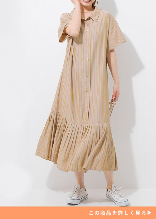裾プリーツデザインのストライプ柄ベージュシャツワンピースを着て、スニーカーを履く女性