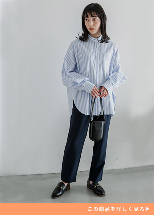 水色のストライプ柄シャツを着て、ネイビーのパンツを履く女性