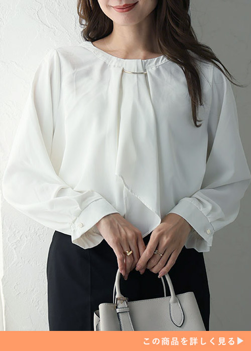 首元にアクセサリーをあしらったホワイトのブラウスを着る女性