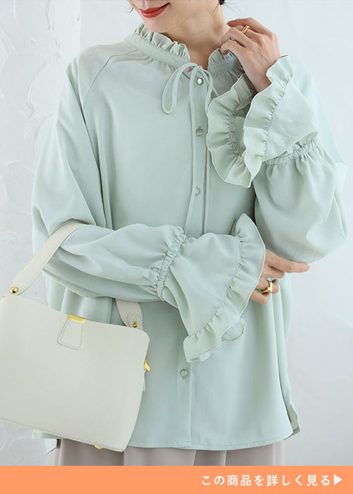 ライトグリーンのフリルブラウスを着て、ベージュのパンツ履く女性