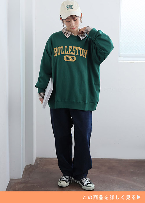 チェック柄シャツにグリーンのロゴ入りトレーナーを重ね着して、デニムパンツを履く女性