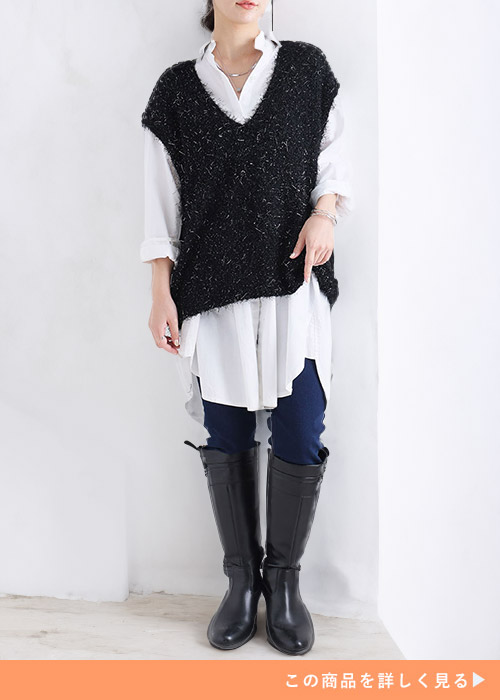 白のロングシャツに黒のフェザーベストを重ね着し、細身デニムパンツとロングブーツを履く女性