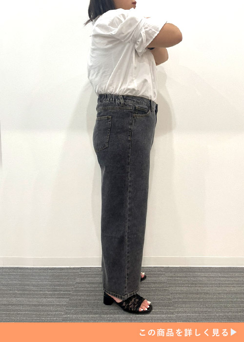 ブラックジーンズを履いて白のフリルシャツを着て横を向く女性