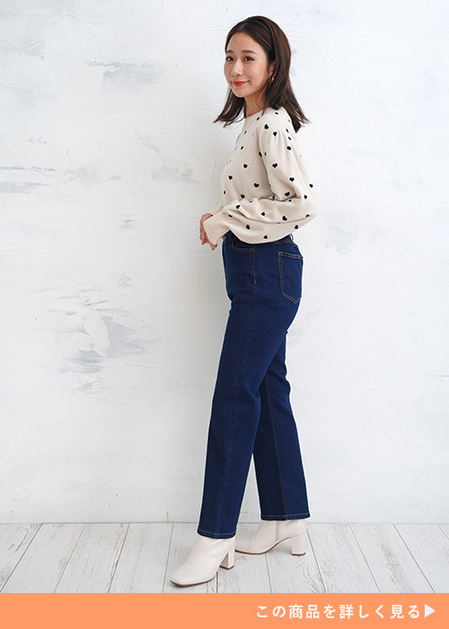ブルーのジーンズにハートドット柄の白トップスを着て横を向く女性