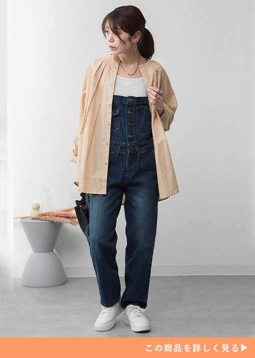 ホワイトトップスとブルーサロペットのコーデにベージュのシャツを羽織る女性