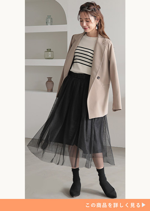 白のボーダー柄ニット×黒のチュールスカートを着て、ベージュのジャケットを肩に掛ける女性