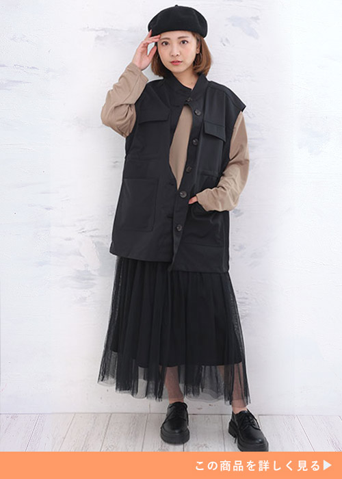 ベージュトップス×黒チュールスカートのドッキングワンピースに黒のミリタリーベストを羽織る女性