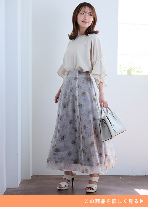 オフホワイトのフリル袖ブラウス×ピンクの花柄オーガンジースカートを着る女性