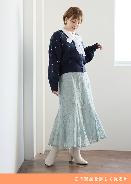 リボンタイブラウスにネイビーカーディガンを着て、グリーンのレーススカートを履く女性