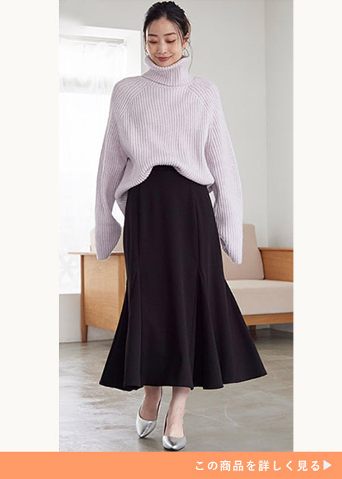 ブラックのマーメイドスカートとオーバーサイズニットのコーデにシルバーパンプスを履く女性