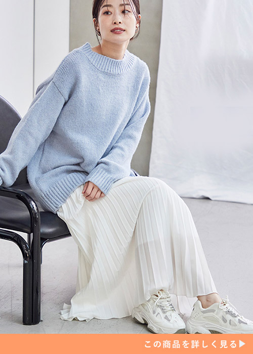 水色のニット×白のプリーツスカートに、白のスニーカーを履く女性