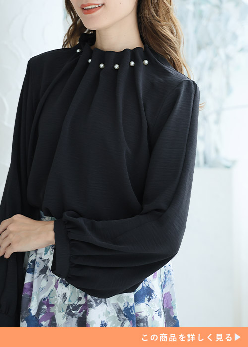 首元にパールをあしらった黒ブラウスを着る女性