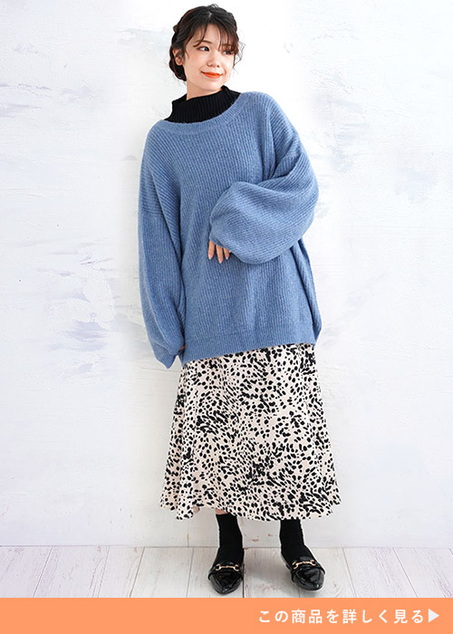黒トップスにくすみブルーのニットを重ね着して、ダルメシアン柄のスカートを履く女性