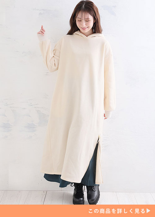 ベージュのフード付きスウェットワンピの下に、緑のプリーツスカートを重ね着する女性