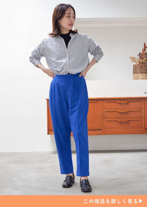 黒トップスにストライプ柄シャツを重ね着して、青のテーパードパンツにトップスインして着る女性