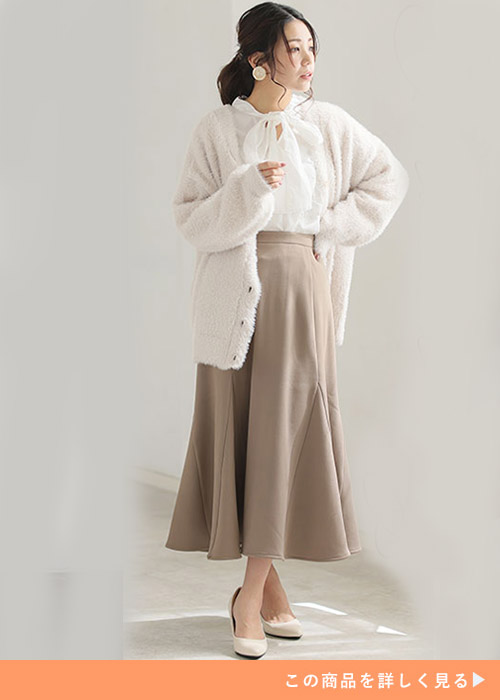 白のリボンタイブラウス×ベージュのマーメイドスカートに、白のカーディガンを羽織る女性
