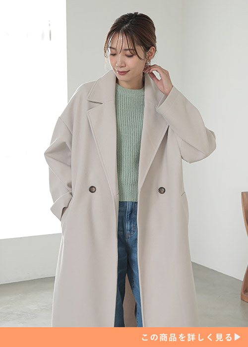 アイボリーのサイドスリットロングコートにグリーンのニットとデニムを履く女性