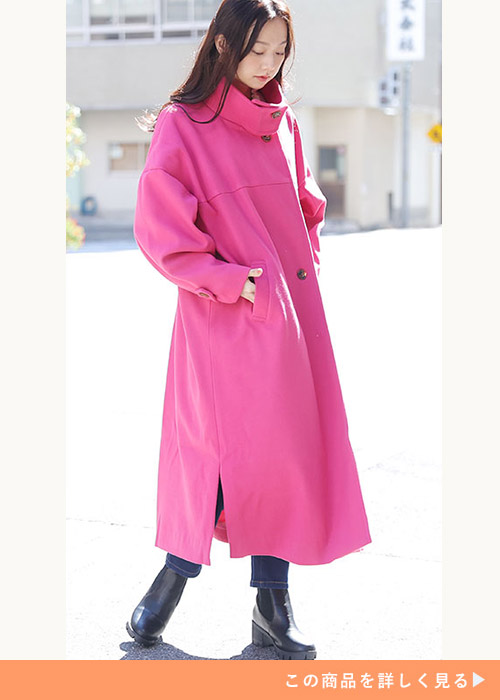 ピンクのスタンドカラーコートにスキニーデニムを合わせ、黒のブーツを履く女性