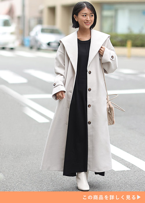 アイボリーのセーラーカラーコートに黒ワンピを合わせ、白のブーツを履く女性