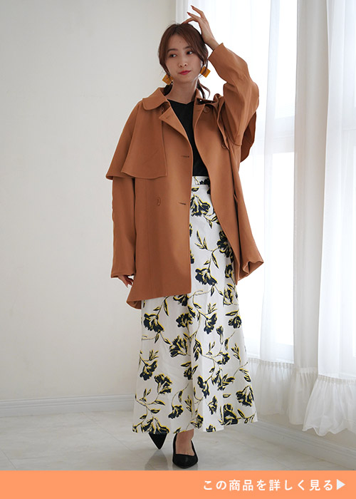 ブラウンのケープコートに、黒のニットと花柄のスカートを履く女性