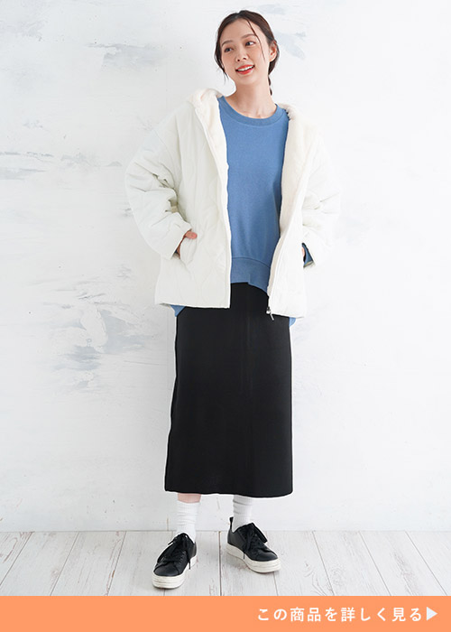 アイボリーのフェイクファーキルトジャケットにブルーニットと黒のナロースカートを合わせる女性